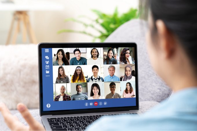 Eine junge Frau bedient in einer
gemütlichen Atmosphäre ihren
Laptop. Im Fokus des Bildes ist der
Bildschirm, auf dem ein virtuelles
Video-Gespräch mit 15 Personen zu
sehen ist.